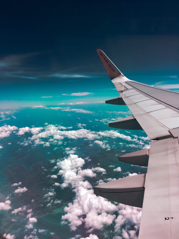 gallery-02 Aerial view of airplane wing over fluffy clouds with a deep turquoise sky.