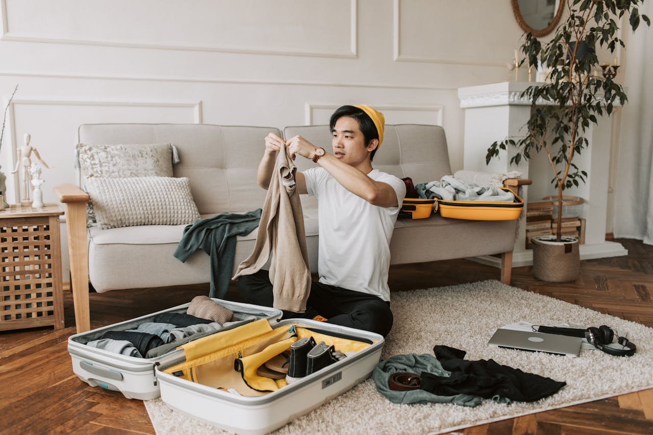 gallery-01 A young man organizes clothes into a suitcase in a stylish living room, preparing for a trip.